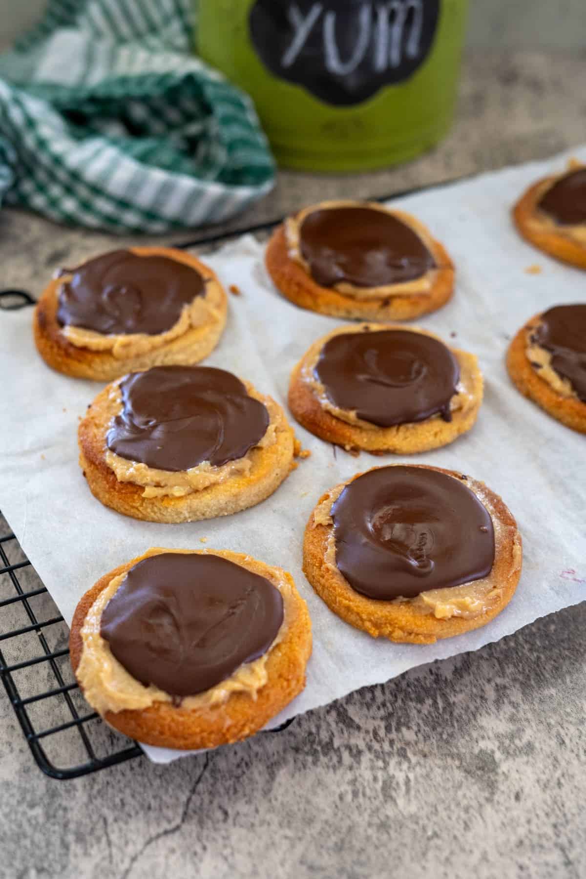 Cookies with a layer of chocolate and peanut butter are on a cooling rack covered with parchment paper.