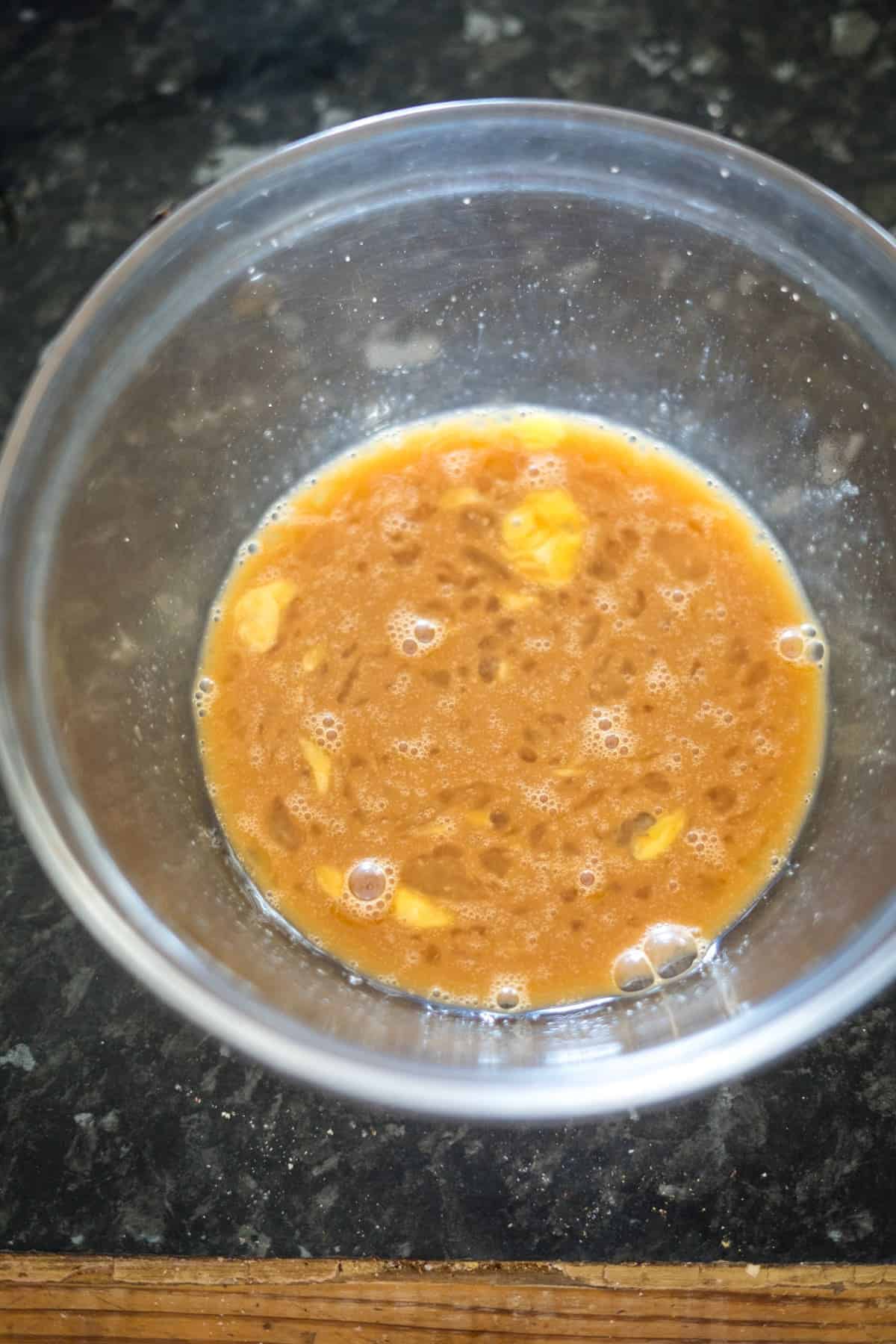 A clear bowl filled with a mixture of beaten eggs and soy sauce sits on a dark countertop, echoing the simplicity of low-carb cuisine.