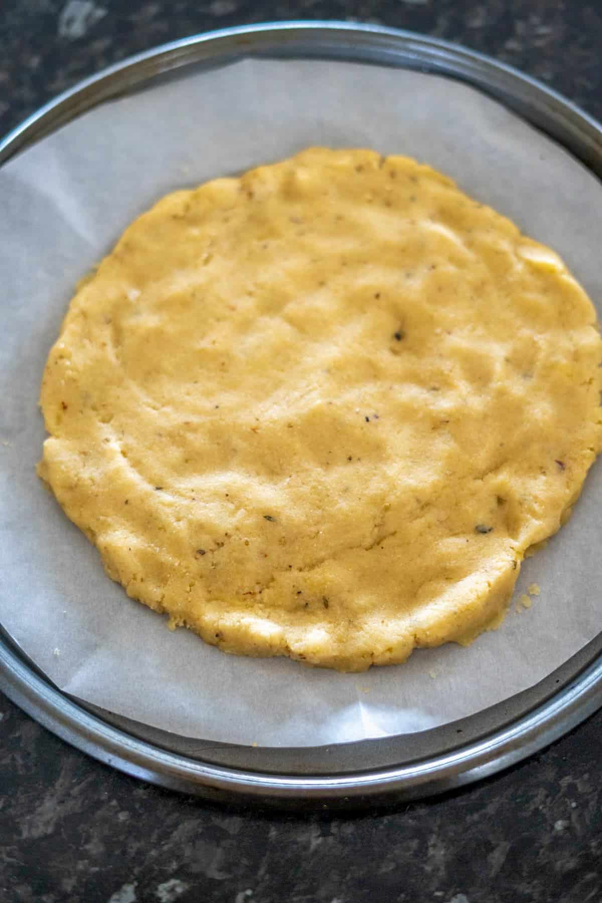 A round, flattened circle of almond flour dough rests on parchment paper, placed on a baking tray.