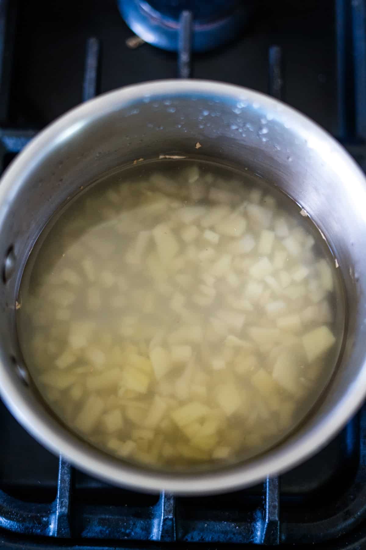 Chopped onions simmering in a pot of water on a stove.