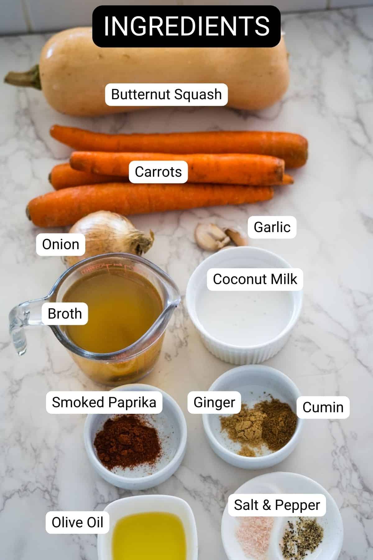 Ingredients on a marble surface: butternut squash, carrots, garlic, onion, broth, coconut milk, smoked paprika, cumin, ginger, salt, pepper, and olive oil.