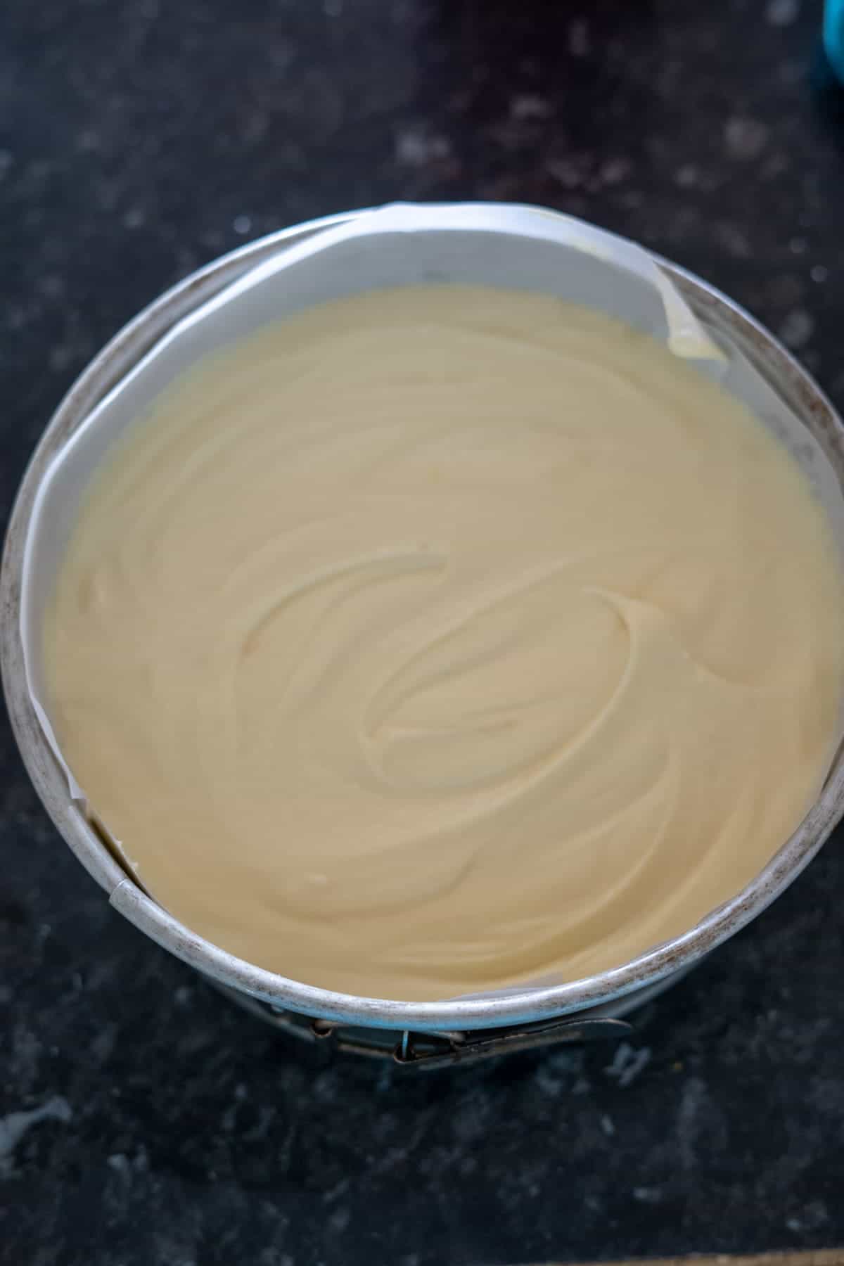 Cake batter in a round metal pan on a dark countertop.