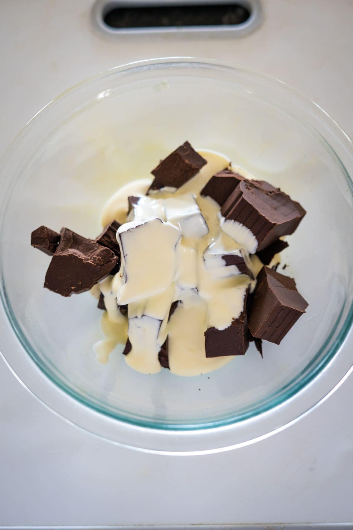 A glass bowl containing chunks of chocolate and a creamy liquid.