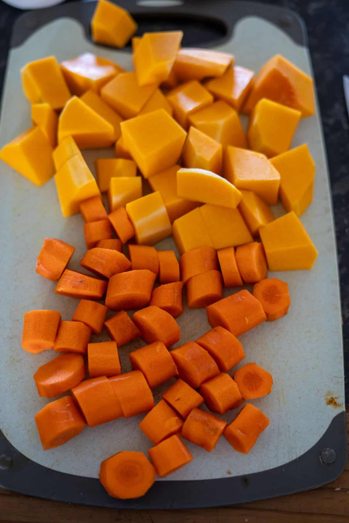 Chopped orange butternut squash and carrots on a cutting board, ready to be transformed into a delicious butternut squash and carrot soup.