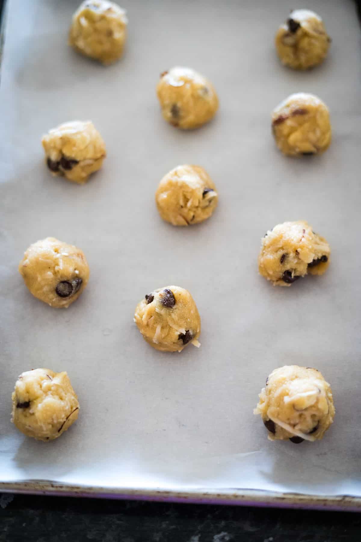 Twelve cookie dough balls on a parchment-lined baking sheet, ready for baking.