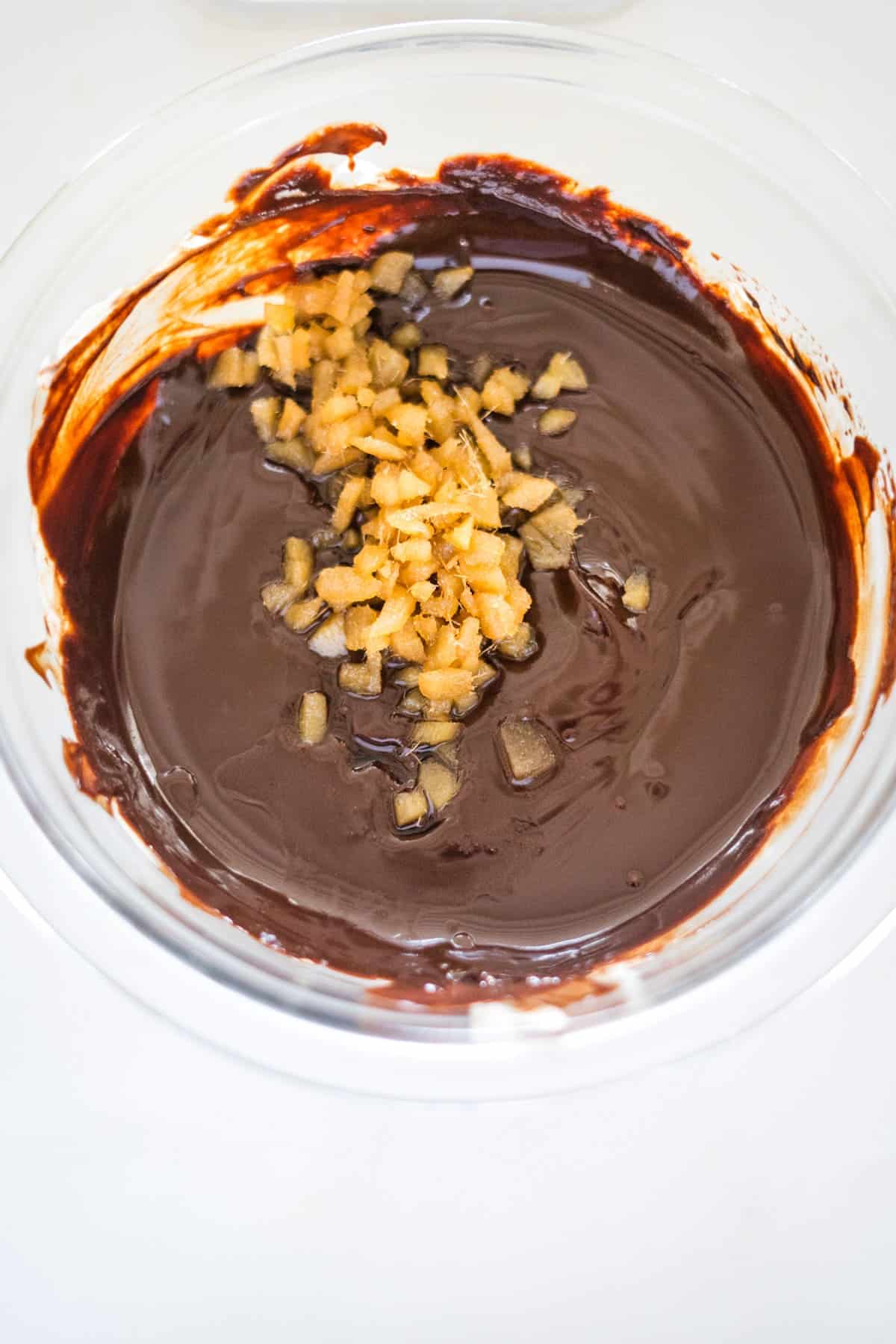 A bowl of melted chocolate mixed with small pieces of candied ginger.