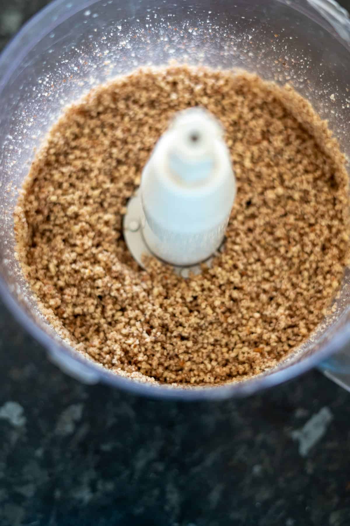 Close-up of ground flaxseed in a food processor on a dark countertop.