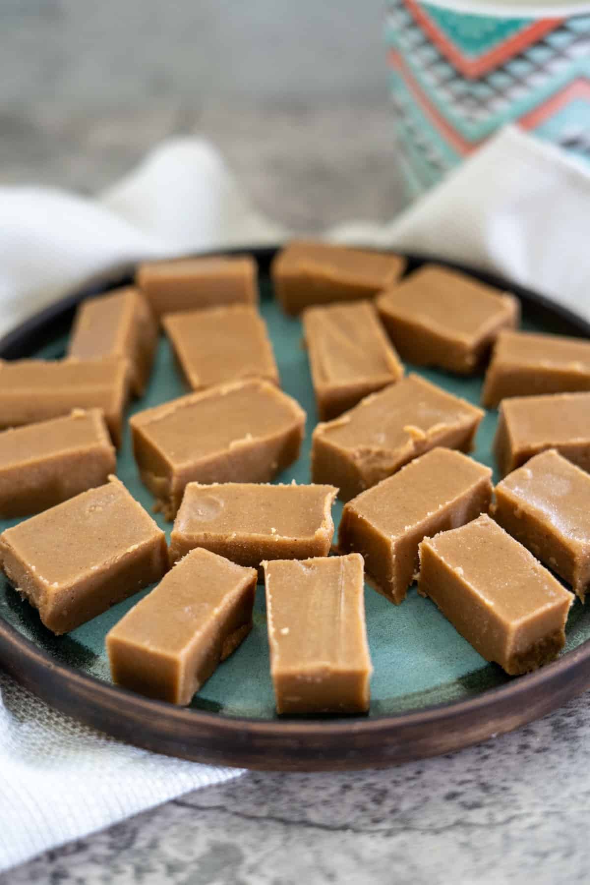 A plate of rectangular keto peanut butter fudge pieces arranged neatly on a blue-green plate, with a patterned jar in the background.