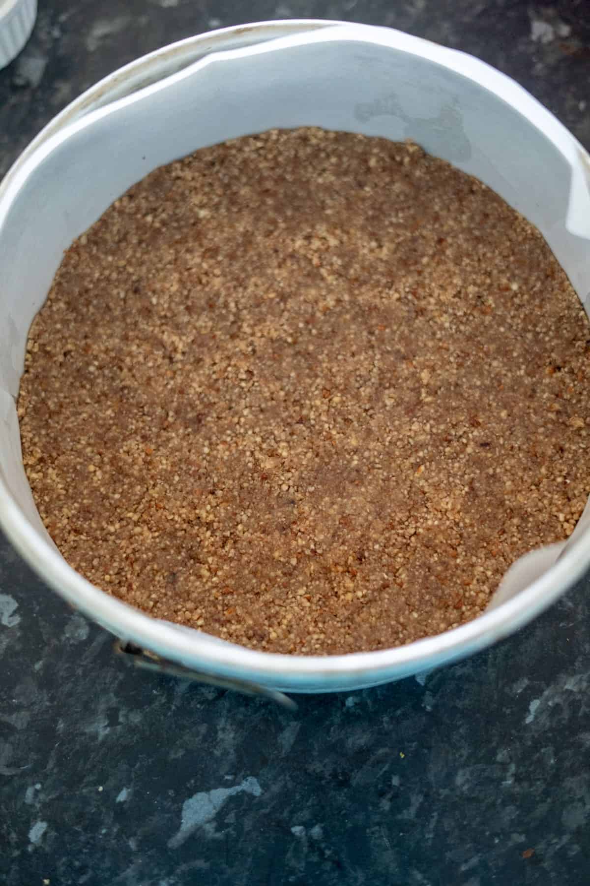 A round baking dish with a layer of crumbly brown crust on the bottom, lined with parchment paper.