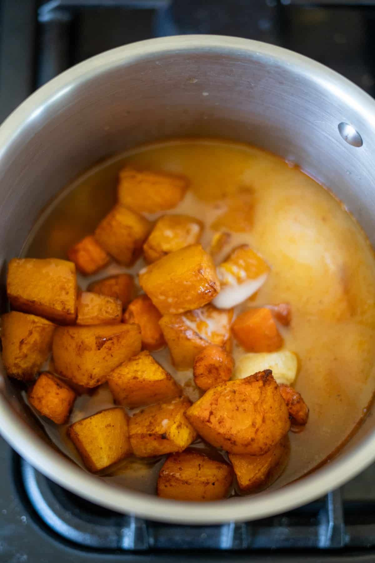 Chunks of roasted butternut squash and vibrant carrots are simmering together in a pot on the stove, creating a warm, comforting soup.