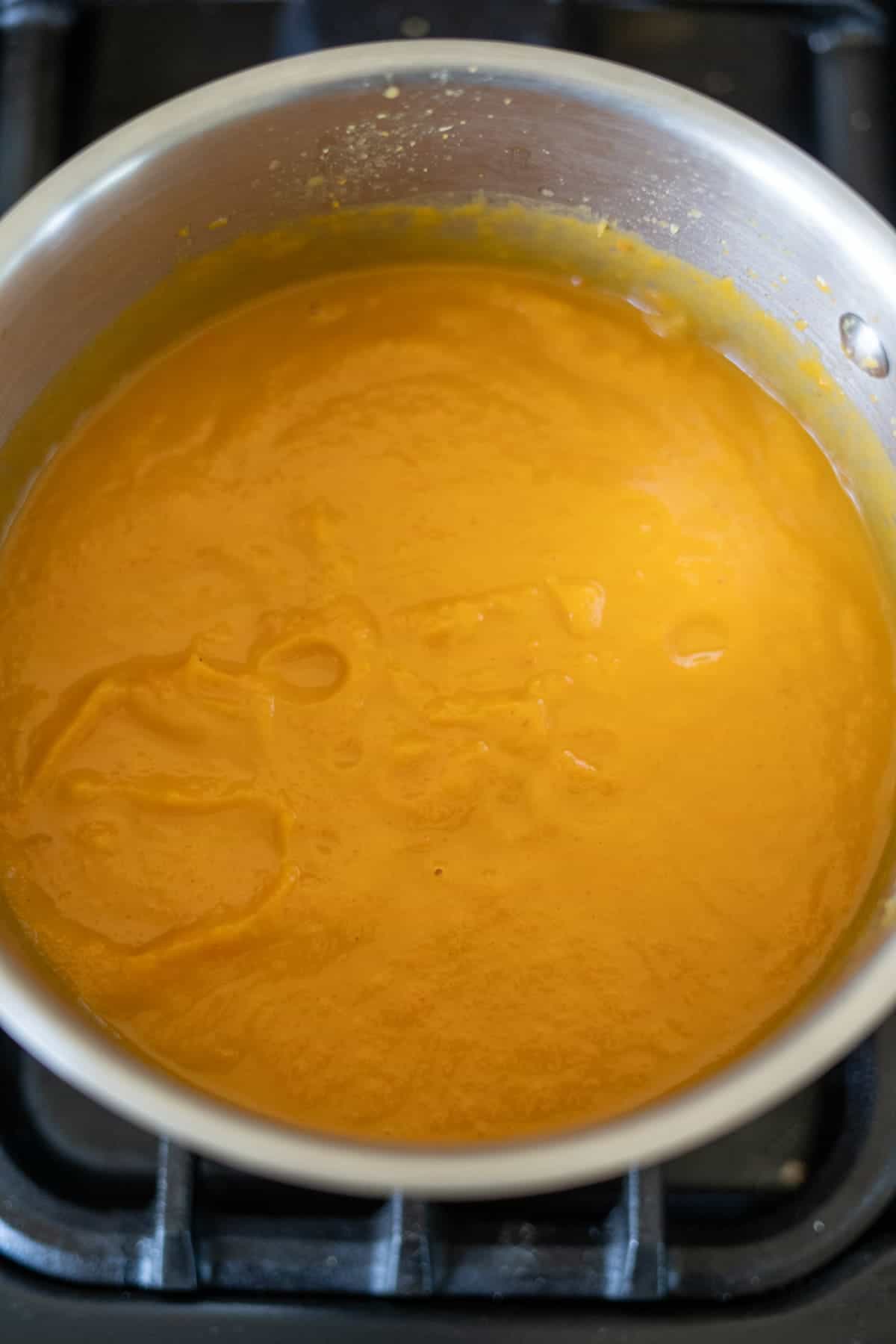 A pot of smooth, orange butternut squash and carrot soup simmers gently on the stovetop.