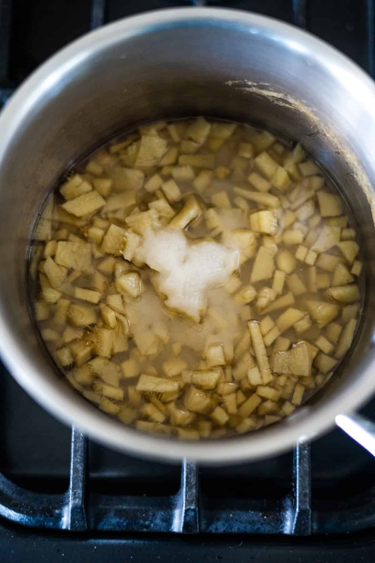 A pot on a stove contains diced ginger boiling in water.