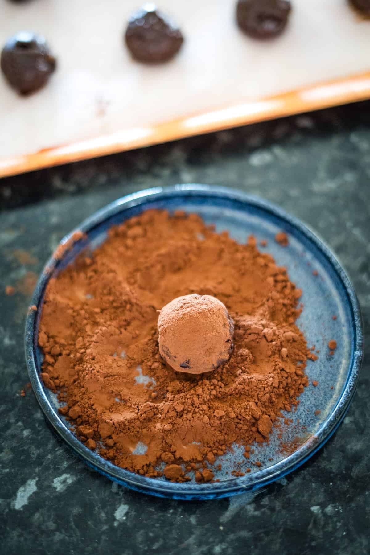 A chocolate truffle is being coated in cocoa powder on a blue plate.